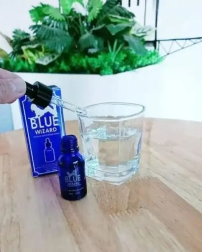 Blue Wizard 15ml kích dục nữ chính hãng – tay nhỏ giọt từ lọ Blue Wizard vào ly nước trên bàn gỗ