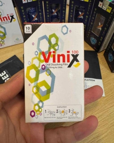 Tem ngậm Vinix 100mg Hàn Quốc chính hãng – tay cầm hộp Vinix 100 trắng đỏ, nền có nhiều hộp khác