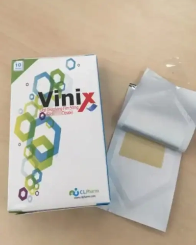 Tem ngậm Vinix 100mg Hàn Quốc chính hãng – hộp Vinix và gói film mở ra lộ miếng film vàng trên bàn gỗ