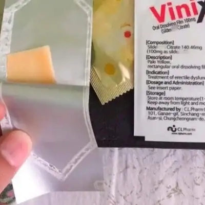 Tem ngậm Vinix 100mg Hàn Quốc chính hãng – tay cầm gói Vinix mở ra lộ miếng film vàng vuông