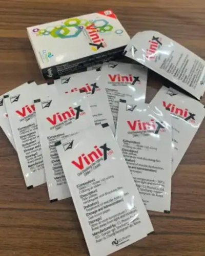 Tem ngậm Vinix 100mg Hàn Quốc chính hãng – hộp Vinix và khoảng mười gói lẻ xòe ra trên bàn gỗ